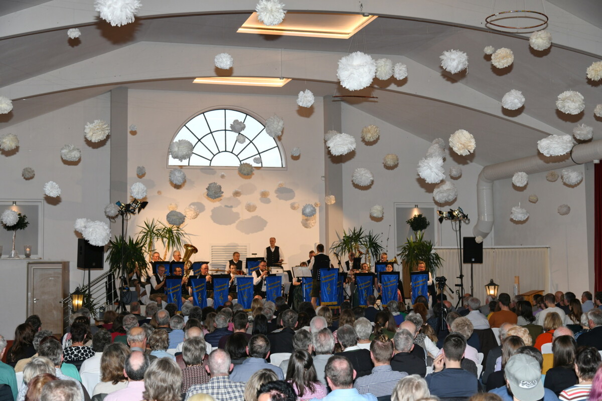 Publikum und Blaskapelle im Konzertsaal, die Decke ist geschmückt mit wolkenähnlichen Wattebauschen