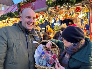 Christoph Maul hat einen Korb mit Sternen und Spendendose in der Hand, eine Dame sucht sich einen Stern aus.