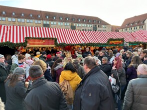 Eine große Menschenmenge vor dem Sternstunden-Stand. Mittendrinnen das aktuelle Nürnberger Christkind in traditionellem Gewand mit blonden Locken und goldener Krone auf dem Kopf.