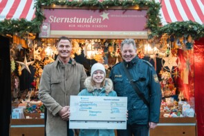 Zwei große Herren von der Polizei überreichen einen überdimensionalen Scheck an Caroline Nieder-Müller von Sternstunden vor dem Sternstunden-Stand.