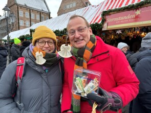 Volker Heißmann rechts und eine Marktbesucherin links haben sich Notenblattengel an den Brillenbügel gehängt und lächeln in die Kamera.