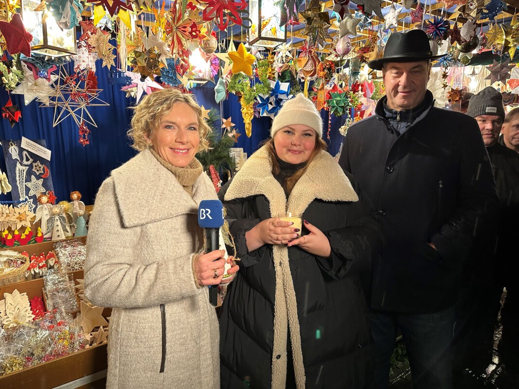 Die Moderatorin Julia Büchler, Felice Schmidt und Dr. Markus Söder stehen vor dem Sternstundenstand. Über ihnen hängen viele farbenfrohe Sterne in allen Größen und Formen.