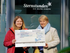 Mona Stangl, Öffentlichkeitsarbeit, nimmt symbolischen Scheck von Irene Rüdel, Vorstandsmitglied von Nähen hilft! e.V., entgegen.
