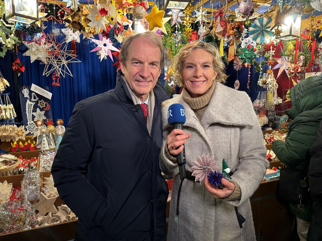 Thomas Jansing und Julia Büchler lächeln in die Kamera, hinter ihnen der Sternstunden-Stand.