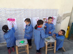 Fünf Schulkinder in blauen Kitteln malen Bilder