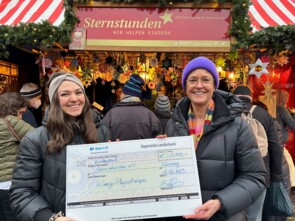 Anna-Maria Brätz und Beate Merz von Sternstunden halten einen überdimensionalen Scheck zu Spendenübergabe am Sternstunden-Stand.