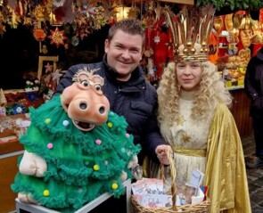 Sebastian Reich mit Amanda, die ein grünes Weihnachtsbaumkostüm trägt, gemeinsam mit dem Nürnberger Christkind vor dem Sternstunden-Stand 2022.
