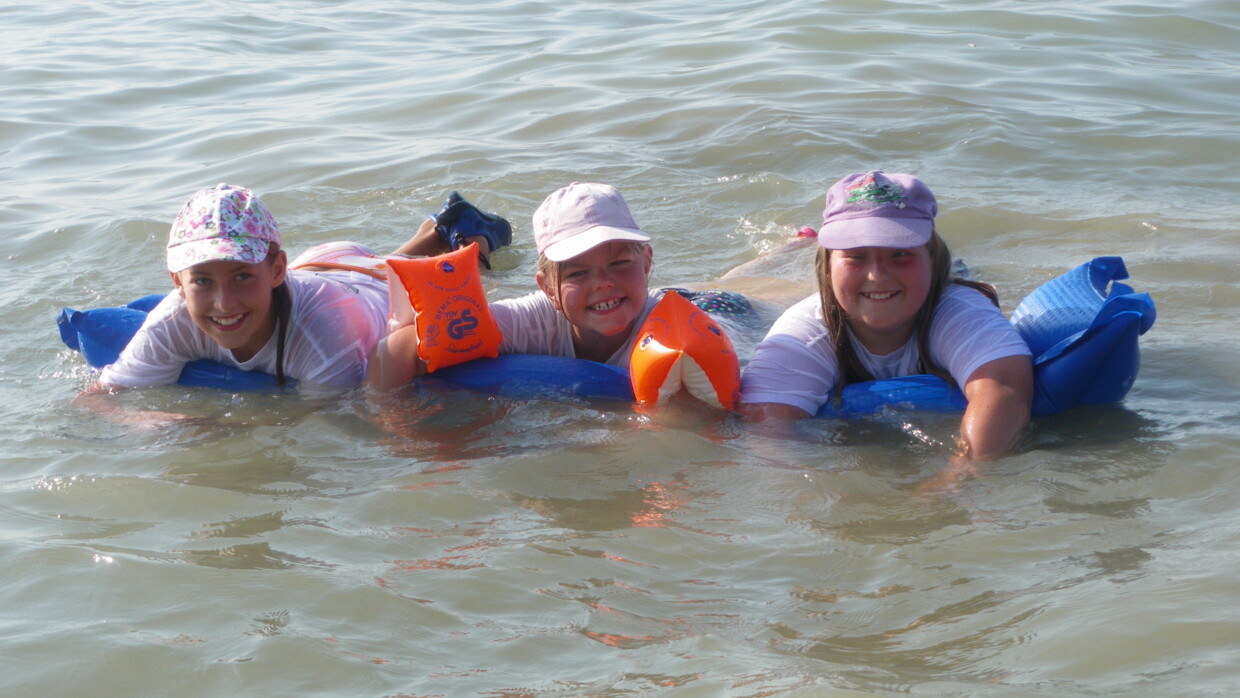 Drei Mädchen liegen auf Luftmatratze im Wasser und lachen in die Kamera