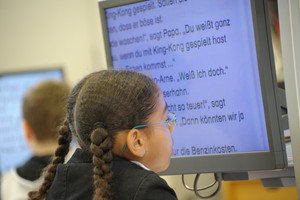 Overshoulder Mädchen mit Brille liest extragroßen Text auf Bildschirm