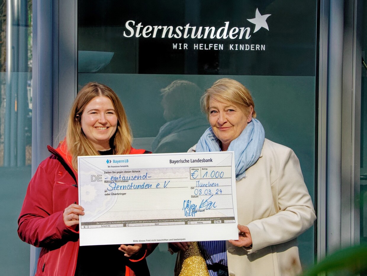 Mona Stangl, Öffentlichkeitsarbeit, nimmt symbolischen Scheck von Irene Rüdel, Vorstandsmitglied von Nähen hilft! e.V., entgegen.