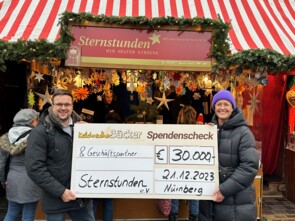 Johannes Wiehgärtner übergibt einen besonders überdimensionalen Spendenscheck über 30000 Euro an Beate Merz von Sternstunden vor dem Sternstunden-Stand.