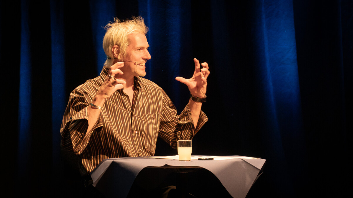 Andreas Dirscherl auf der Bühne, liest vor und gestikuliert mit den Händen.