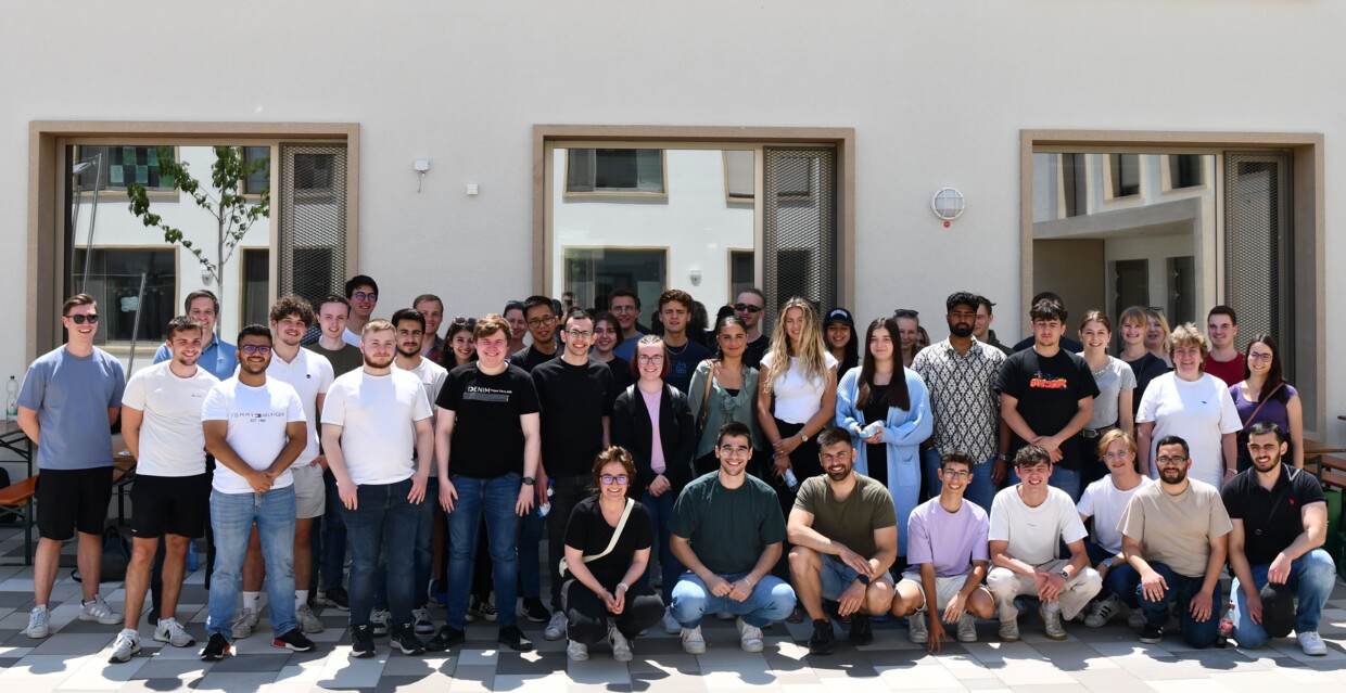 Ein Gruppenfoto mit allen 54 Azubis und ihren Ausbildenden vor einer weißen Hauswand bei Sonnenschein.