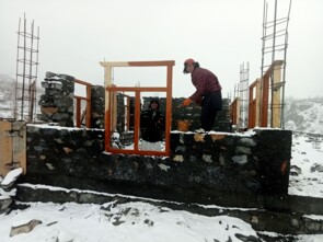 Zwei Männer bauen bei Schnee, Nebel und Kälte an den Grundmauern der neuen Schule.