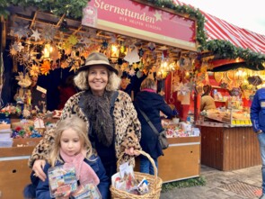 Michaela May mit ihrer kleinen Enkelin vor dem Stand. Sie halten einen Korb und zwei volle Spendendosen in die Kamera. Die Enkelin schaut nicht direkt in die Kamera, sondern auf die beiden Spendendosen.