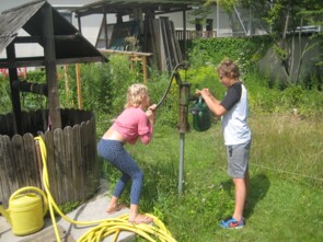 Ein Junge und ein Mädchen pumpen Wasser in eine Gießkanne im Garten des Kinderheims.