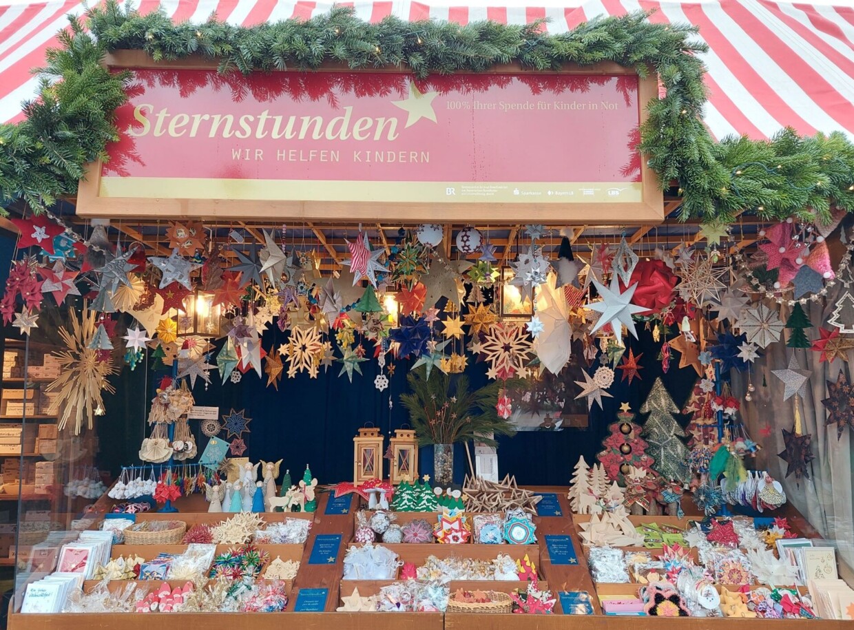 Der Sternstunden-Stand auf dem Christkindlesmarkt in Nürnberg in seiner vollen Pracht. Dekoriert mit von der Decke hängenden Sternen und auch in den Auslagen liegen viele Sterne und andere Dekorationen.
