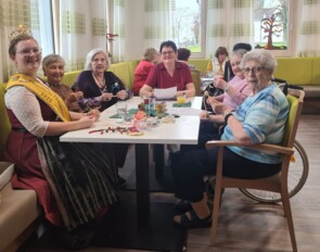 Die Honigprinzessin sitzt mit Seniorinnen am Tisch und bastelt Sterne für den guten Zweck.