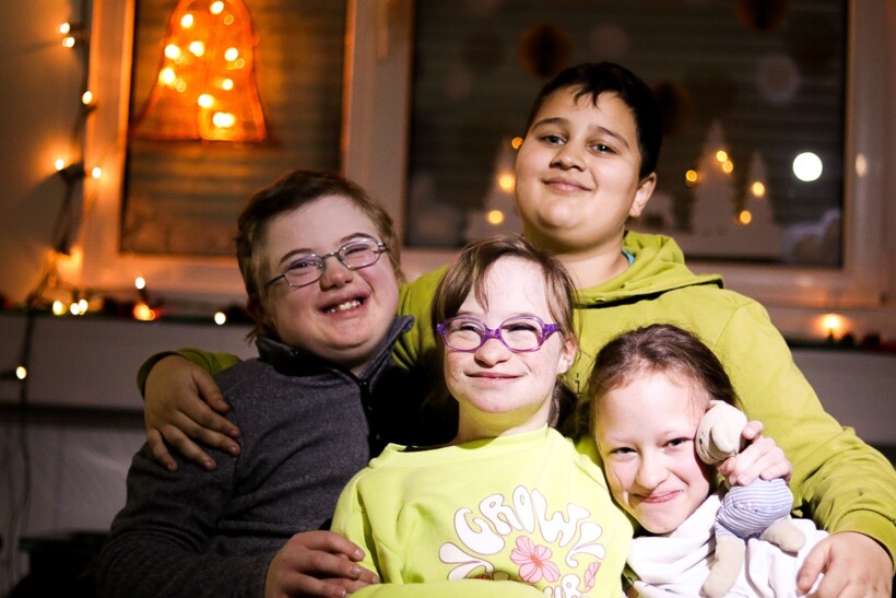 Vier Kinder sitzen eng zusammen und halten die Arme umeinander. Sie lachen in die Kamera.