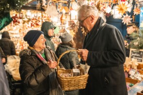 Eine Marktbesucherin strahlt Joachim Herrmann an als sie sich einen Stern aus dessen Körbchen nehmen darf.