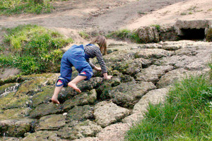 Mädchen (Rückansicht) klettert kleinen Bachlauf mit Steinen hoch
