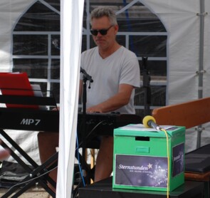 Mann am Klavier, im Vordergrund eine grüne Spendenbox mit Sternstundenaufkleber