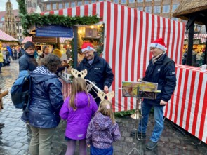 Die BR Heimat Moderatoren unterhalten sich mit einem jungen Mädchen über das Flügelhorn. Das Mädchen und seine Schwester und seine Mutter sind von hinten zu sehen.