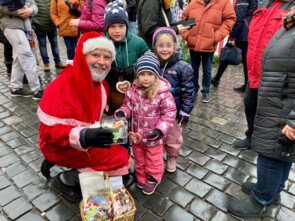 Marcel Schneider als Nikolaus verkleidet hockt sich hin, um mit drei Kindern, zwei Mädchen und einem Jungen, ein Foto zu machen. Alle lächeln in die Kamera. Marcels Spendendose ist schon gut gefüllt.