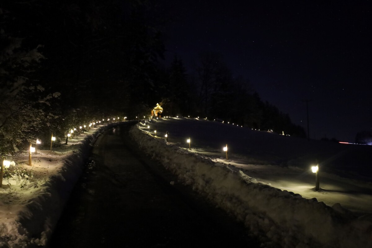 Weg mit Lichter geschmückt vor winterlicher Kulisse.