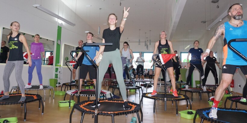 Mehrere Personen springen auf Trampolins, im Vordergrund macht eine Frau das Peace-Zeichen.